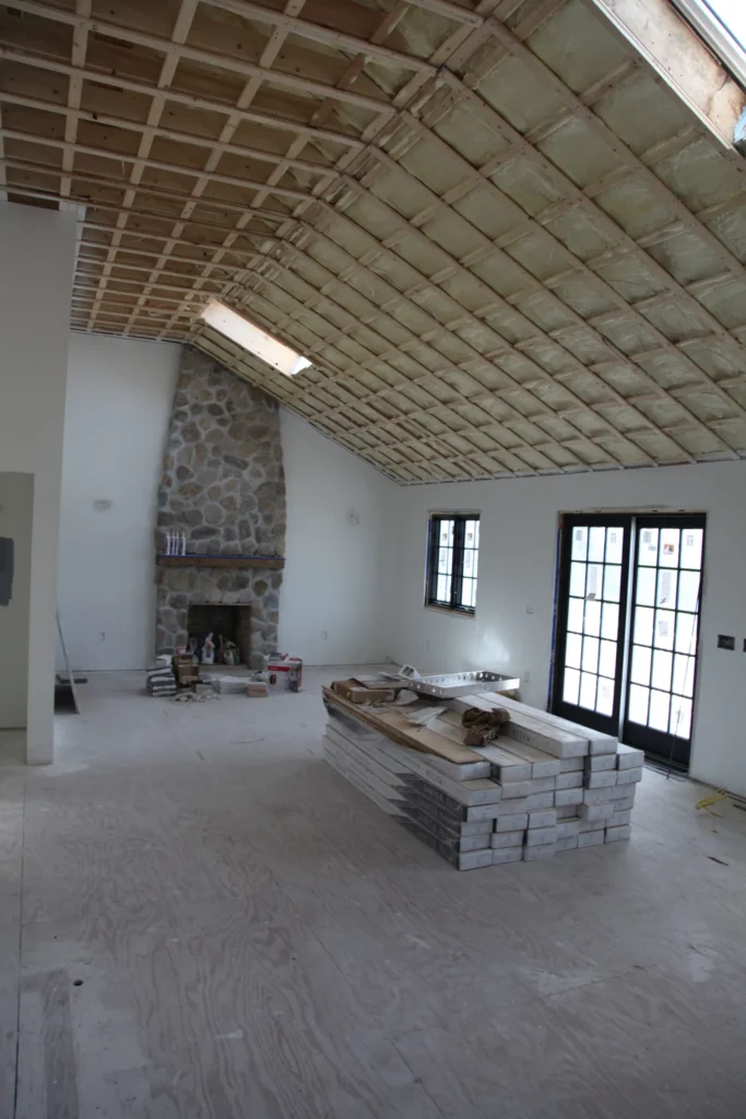Vaulted living room with an exposed ceiling and stone fireplace during renovation in Dennis, MA