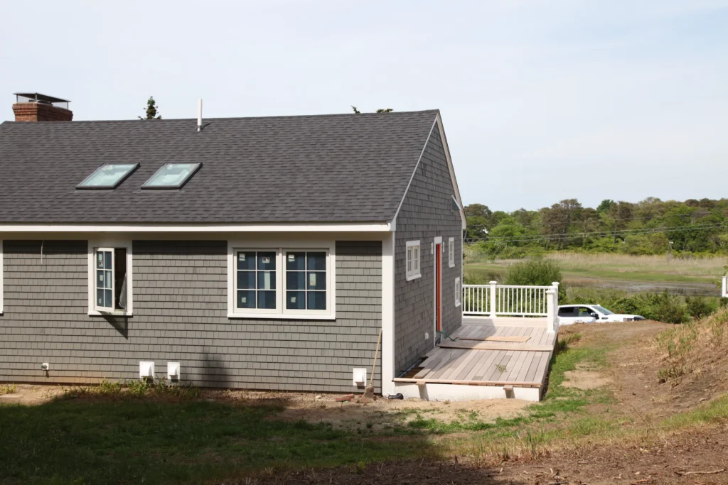 Rear of a gray-shingled Cape home with a deck near marshland in Dennis, MA