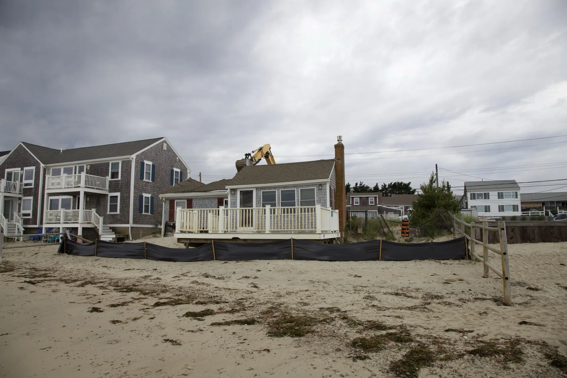 A Custom Crafted Homes beachfront project underway in Dennis Port, MA, with an excavator working on an aging seasonal cottage on the Nantucket Sound shore.