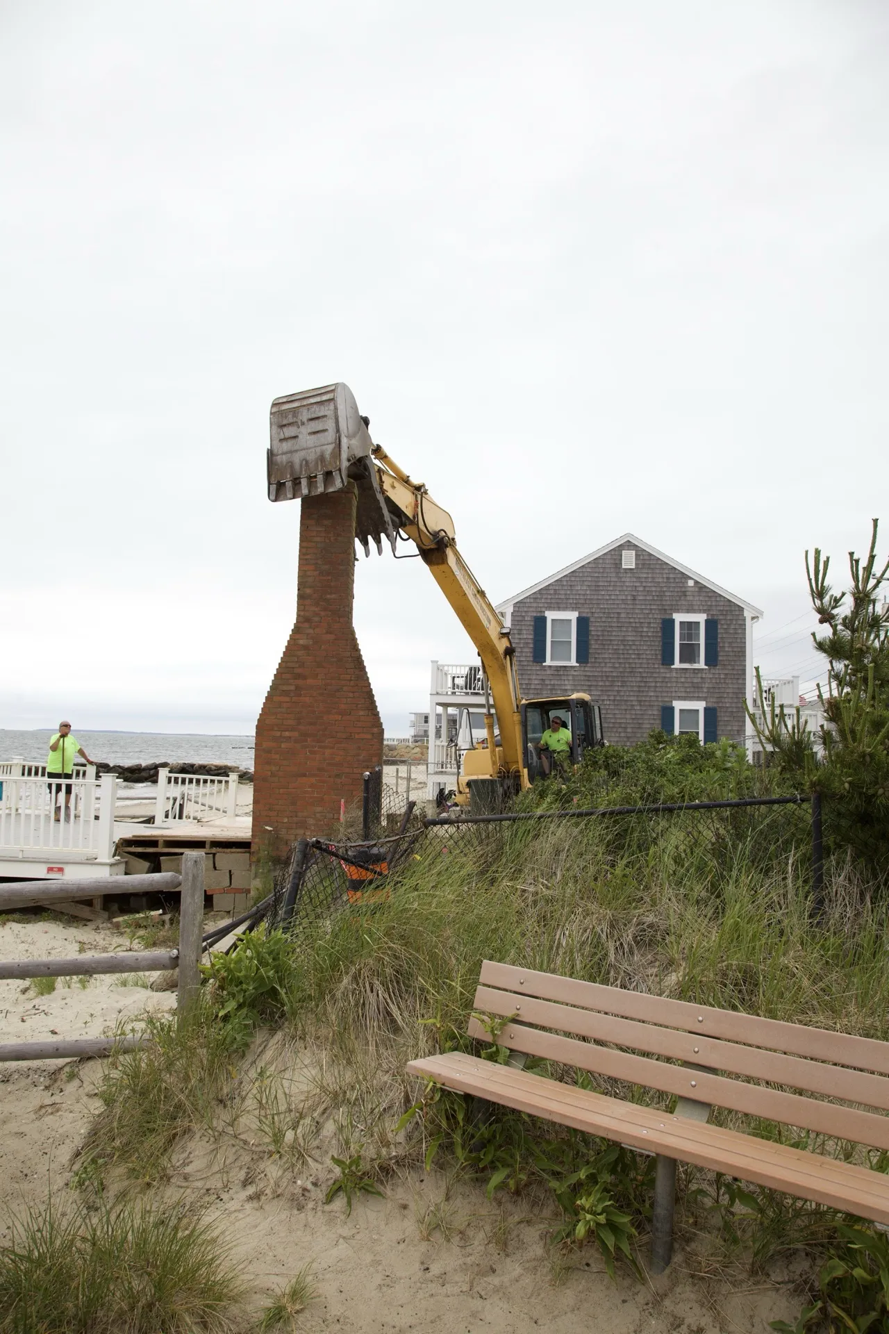 Excavator bucket lifting the top of the old brick chimney against the sky in Dennis Port.