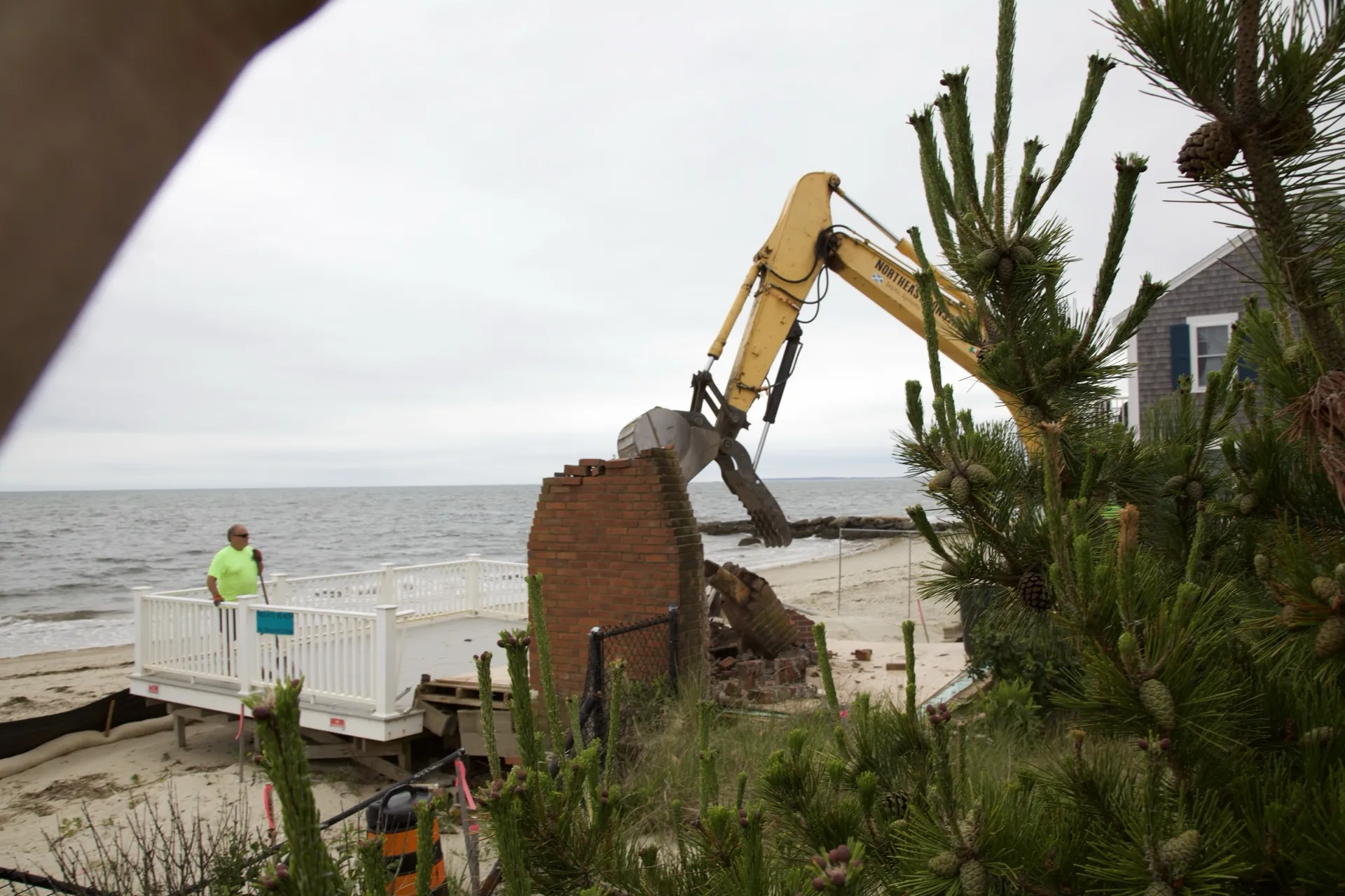 Site crew and excavator framed by a pine, removing the last of a beachfront cottage in Dennis Port.