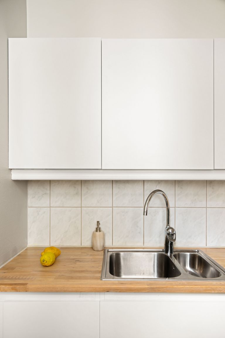 White Cape Cod kitchen with butcher-block counter and stainless sink — kitchen remodel by Custom Crafted Homes