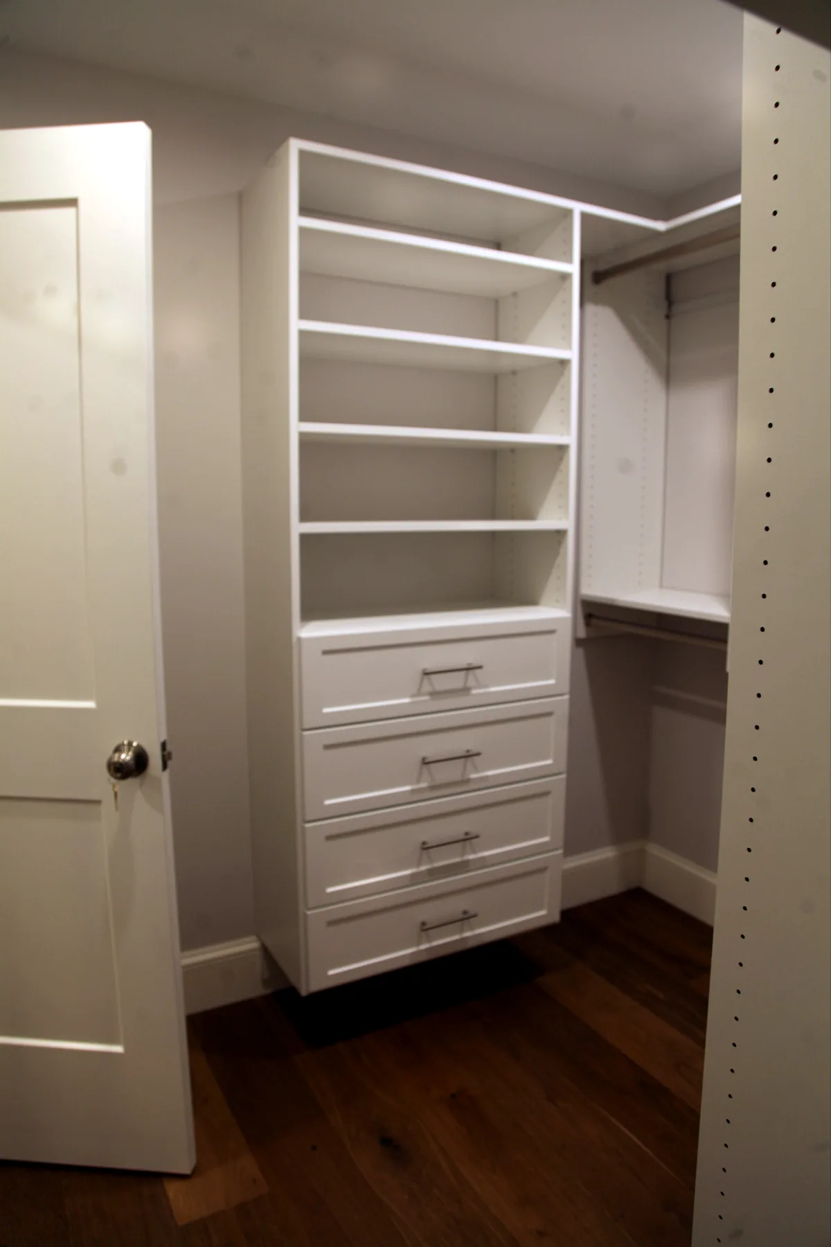 Custom closet built-ins with white shelves, drawers, hanging rods, and wood flooring