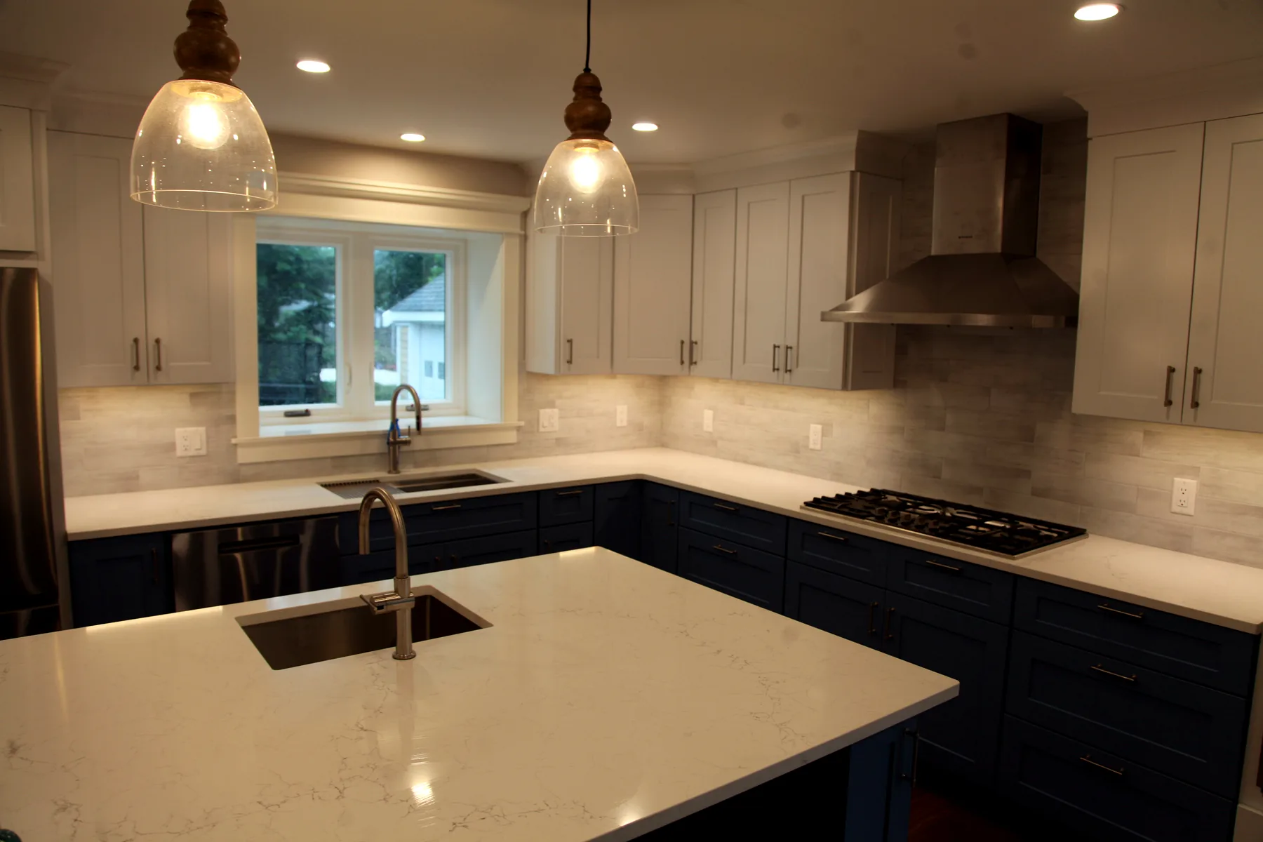 Cape Cod kitchen remodel with large island, blue base cabinets, white upper cabinets, tile backsplash, and range wall