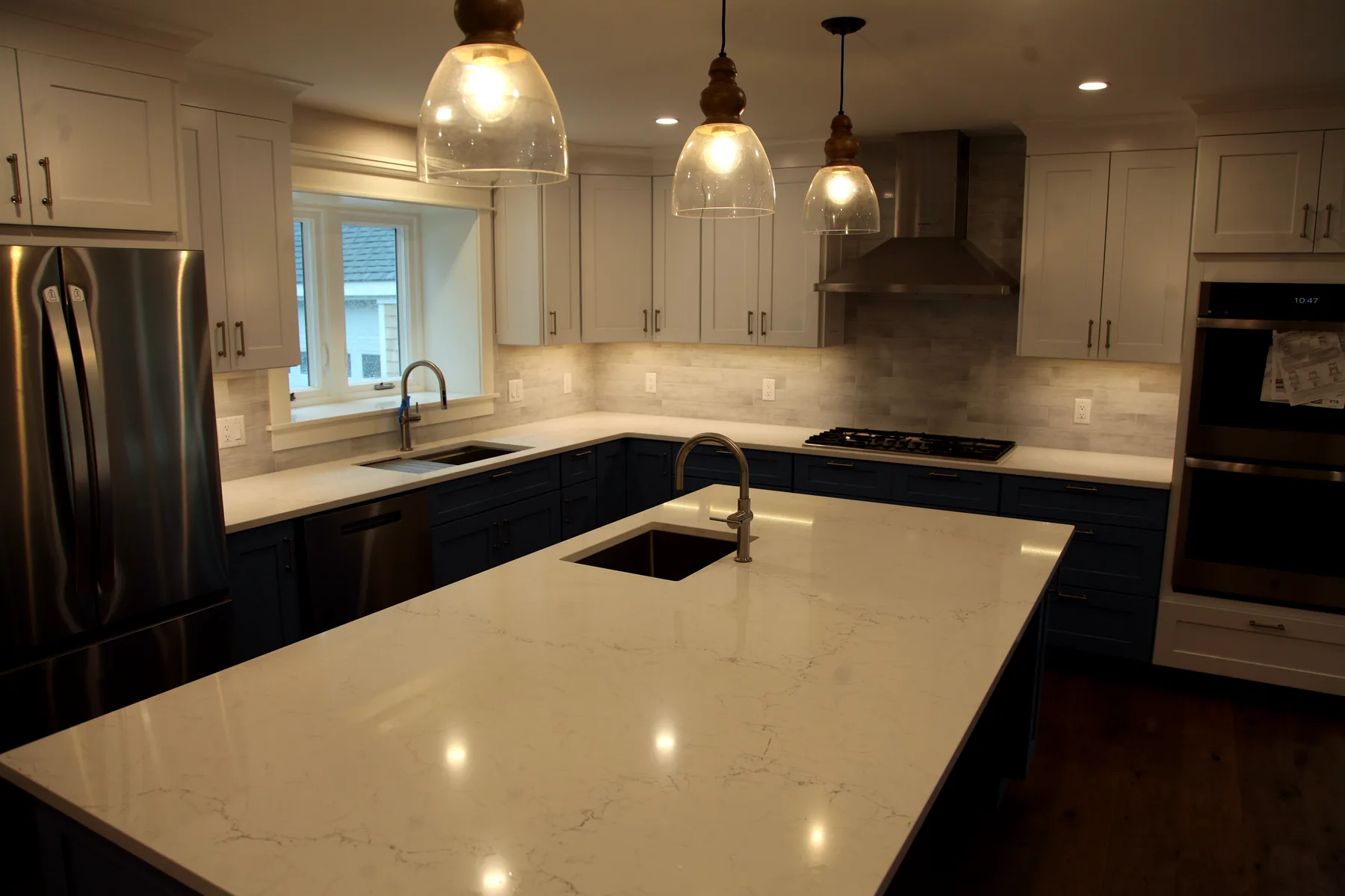 Blue-and-white Cape Cod kitchen remodel with island, quartz counters, pendant lights, and stainless range hood